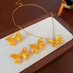 Detailed view of 18K gold plated hollow bow jewelry set on a beige cushion in a wooden tray