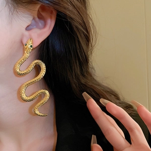 Close-up of long gold snake earrings with green eyes worn by a model in a fashion shot
