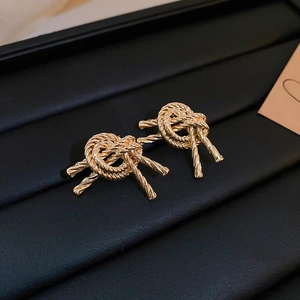 Close-up of golden rope knot stud earrings with textured metallic finish on a black display