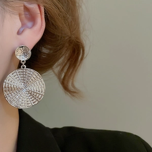 Detailed view of silver dual-disc drop earrings with spiral woven texture on a model