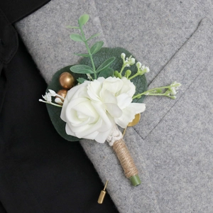 Boutonnière de roses blanches avec eucalyptus et baies dorées sur un revers de costume