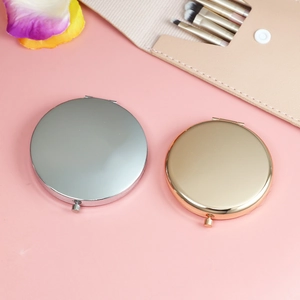 Polished gold and silver metal pocket mirrors displayed on a pink surface with petals