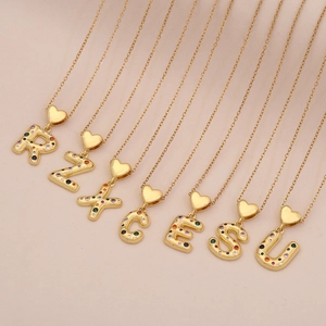 Gold heart letter necklaces with colorful cubic zirconia on soft pink background