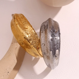 Poliertes Gold- und Silber-Manschettenarmband mit Wassertropfen auf Metalloberfläche