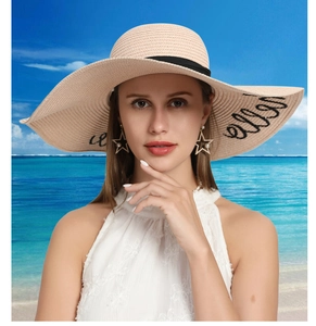 Detail of light beige straw hat featuring wide brim with black ribbon and cursive embroidery