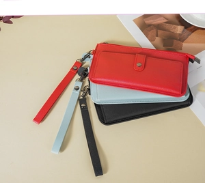Three long leather wallets in red, blue, and black with matching wrist straps on a desk