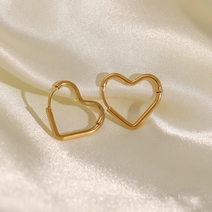 Polished golden stainless steel heart hoop earrings on elegant silk background