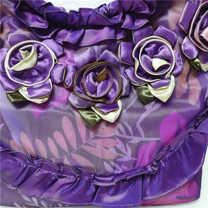 Detailed macro view of purple satin fabric featuring 3D handmade flowers and ruffled mesh