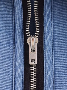 Detailed macro view of silver metal zipper on dark blue denim jacket fabric