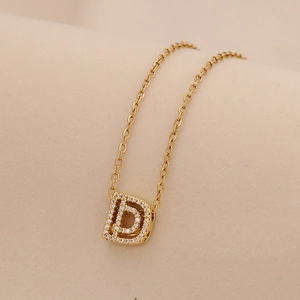 Macro shot of gold D-letter pendant necklace with sparkling cubic zirconia on beige fabric