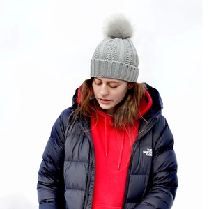 Close-up of light grey knit beanie featuring a large pompom and thick ribbed texture