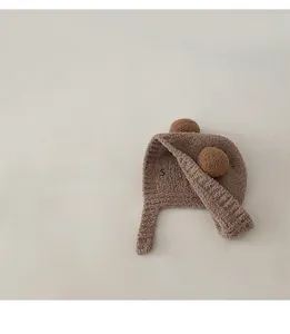 Detail view of plush brown baby earflap hat with fluffy dual pompoms and soft texture