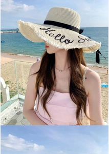 Detail of straw hat with Hello Sunshine embroidery and chic frayed edges on sandy beach