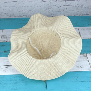 Detail of beige straw sun hat showing wavy brim and elastic chin strap for wind protection