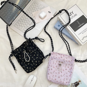 Flat lay of floral canvas mini cross-body bags with adjustable drawstrings and accessories