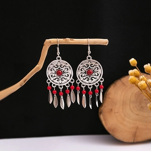 Close-up of bohemian silver earrings featuring intricate filigree and red bead tassels