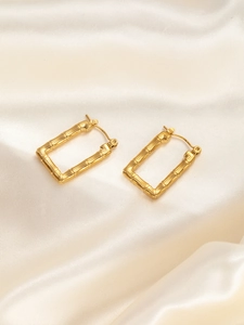 Detail von vergoldeten Ohrringen mit Bambustextur auf elegantem Seidenhintergrund