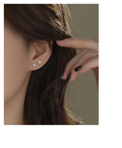 Close-up of a model wearing a small silver eight-pointed star stud earring with tiny crystals