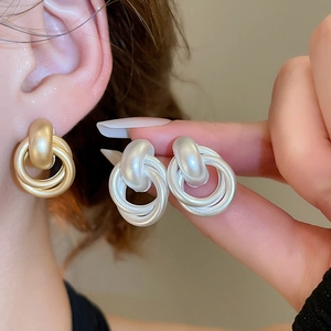 Macro detail of matte gold and silver geometric multi-layer hoop earrings for women