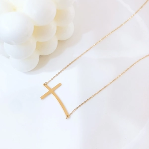 Collana minimalista dorata con ciondolo a croce curva su supporto geometrico bianco