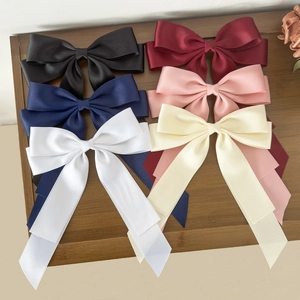 Elegant satin bow hair clips in multiple colors displayed on a wooden tray