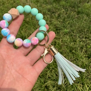 Detail of mint green and tie-dye silicone bead keychain with wood bead and leather tassel