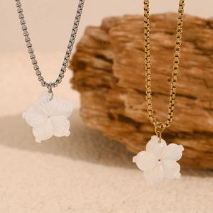 Nahaufnahme von Gold- und Silberketten mit Blumenanhängern auf Naturstein und Sand
