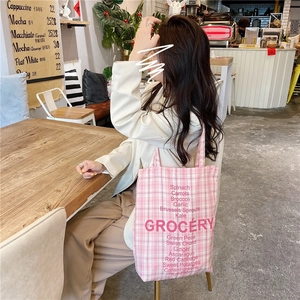 Detail of pink plaid canvas tote bag with GROCERY print carried by a model in a cafe