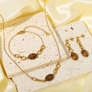 Gold stainless steel jewelry set with brown tiger eye stones on beige stone travertine