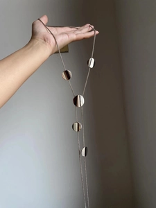 Detail of silver long chain necklace featuring five polished geometric circular pendants