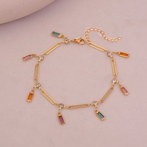 Detailed view of a gold-finish anklet with colorful charms on a soft pink background
