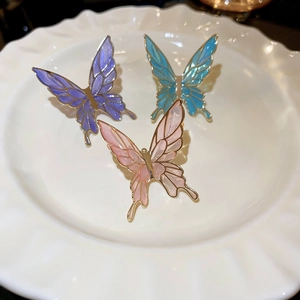 Three colorful vintage enamel butterfly ear clips in gold-tone metal on a ceramic dish