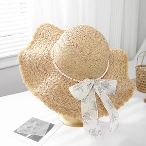 Dettaglio cappello di paglia con catena di perle, nastro floreale e bordo sfrangiato
