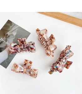 Detail of four acetate bow hair claws with tortoise and marble patterns on white table
