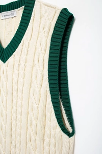 Detailed view of cable knit pattern and contrast green V-neck trim on beige vest