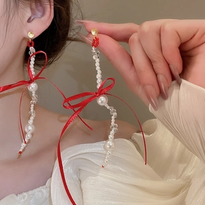 Detailed close-up of elegant long tassel earrings with white pearls and red ribbon bows