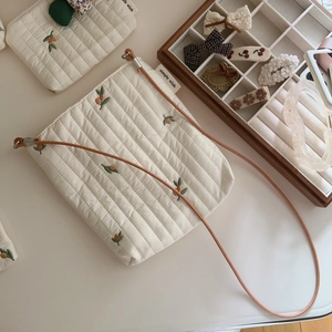 Cream quilted crossbody bag with berry embroidery and a brown slim leather strap