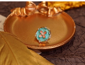 Macro detail of round gold floral brooch with blue enamel and pink rhinestone flower