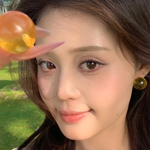 Close-up of a model wearing a translucent amber resin sphere stud earring on a sunny day