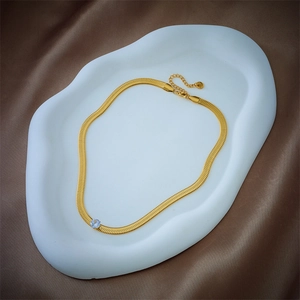 Elegant gold snake chain necklace with a blue round gemstone on a wave display stand