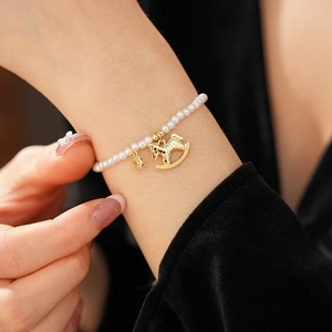 Detail of pearl bracelet featuring golden rocking horse charm and zircon coin pendant