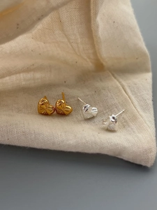 Detailed view of heart-shaped silver and gold stud earrings with bow relief on linen