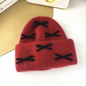 Detail of red knit beanie with black velvet bows on a minimalist white table