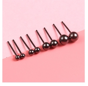 Macro view of four different sizes of polished black metal ball earrings on pink background