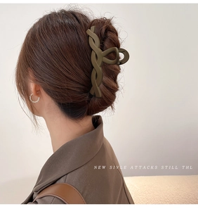 Close-up of a matte dark green hair claw clip with woven texture worn by a model