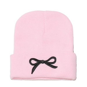 Détail du bonnet en tricot rose avec un nœud noir brodé sur le rebord replié