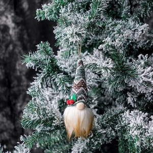 Christmas gnome pendant with green knitted hat and white beard hanging on snowy tree