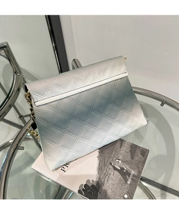 Dettaglio della borsa a tracolla trapuntata sfumata blu con catena dorata su tavolo in vetro