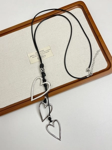 Detail of three tiered metallic hollow heart pendants on an adjustable black cord necklace