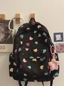 Black canvas backpack with colorful bear prints and flower pendant on white wall